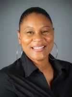 Professional headshot of a smiling woman with pulled-back hair wearing a black shirt against a gray background.