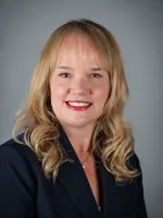 Professional headshot of a woman with blonde wavy hair and red lipstick wearing a dark blazer.