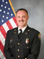 Law enforcement officer in uniform standing in front of American flag.