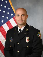 Man in dress uniform standing in front of American flag.